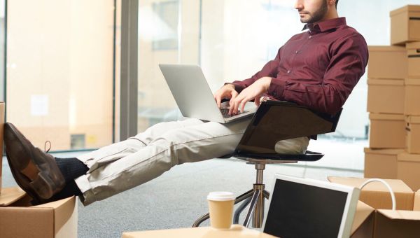 Male business owner in stock room typing on laptop with coffee